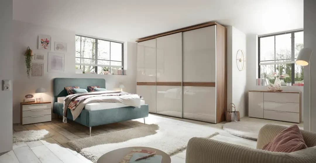 Helles Schlafzimmer mit einem großen Bett, einem Kleiderschrank, Nachttischen und einem gemütlichen Sessel.