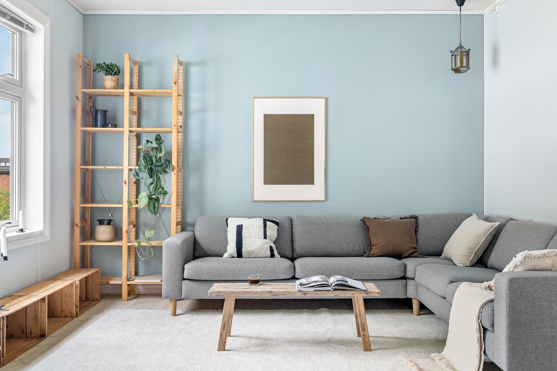 Helles skandinavisches Wohnzimmer mit grauem Ecksofa, Holzregal und aufgeschlagenem Magazin auf dem Couchtisch