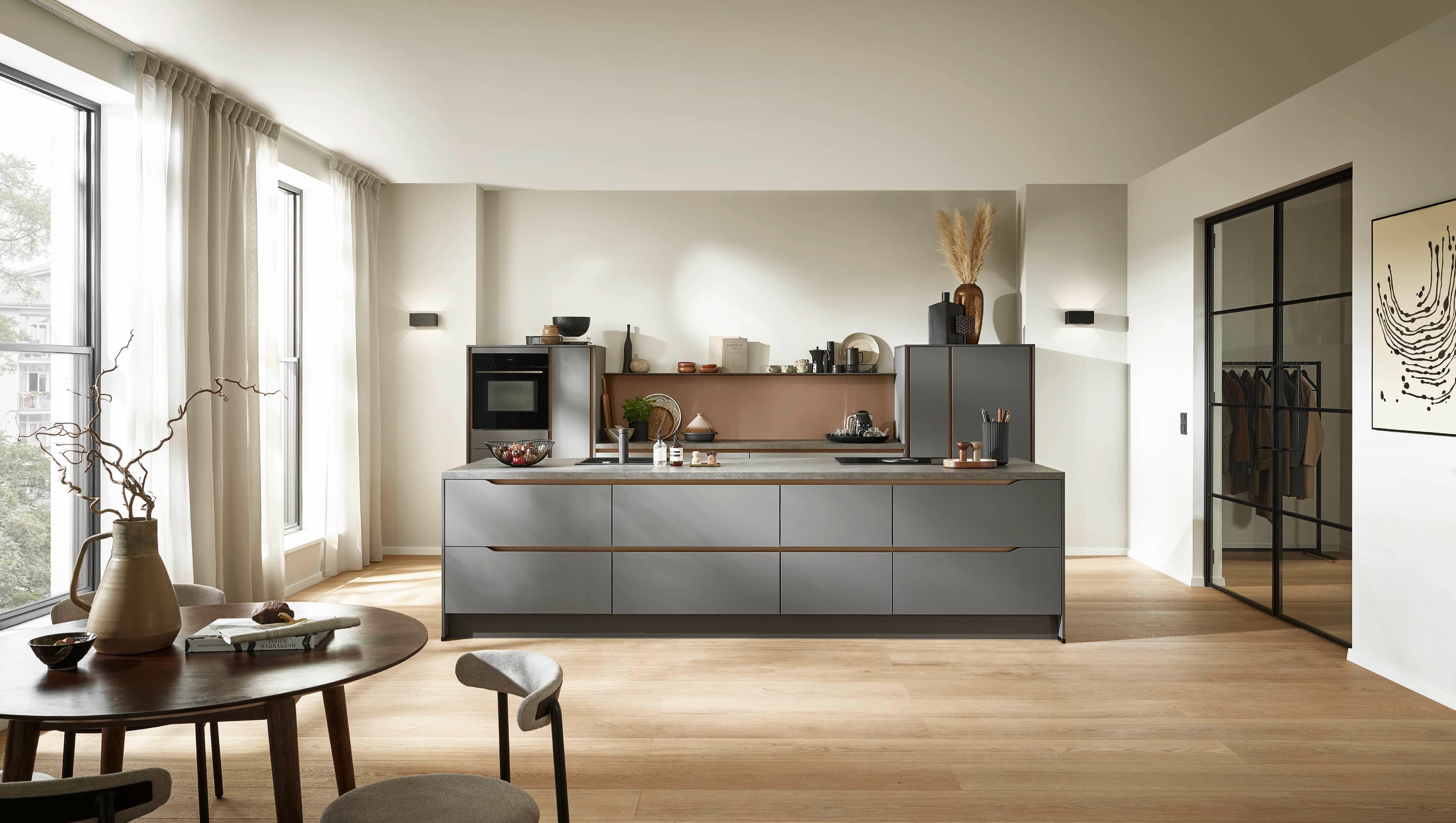 Moderne Küche mit grauen Schränken, Holzdetails und großem Fenster, ergänzt durch einen Esstisch und Stühle.