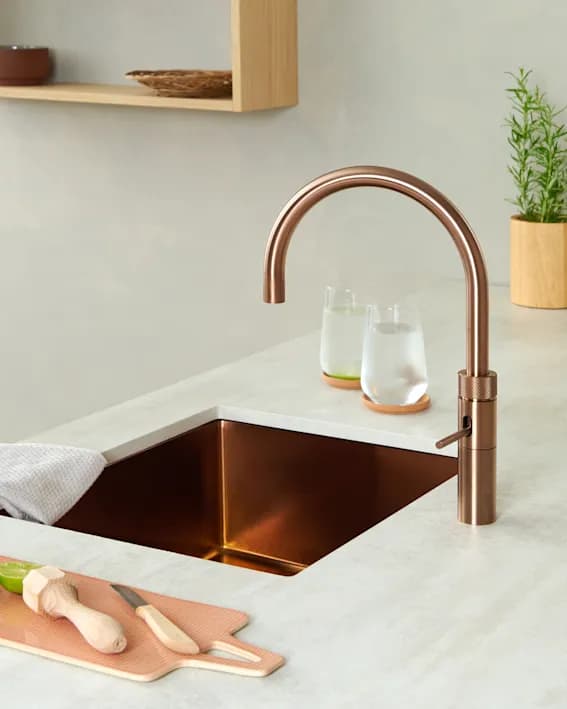 Moderne Küche mit kupfernem Wasserhahn, darunter ein kupferner Spülbecken und frischen Kräutern auf der Ablage.