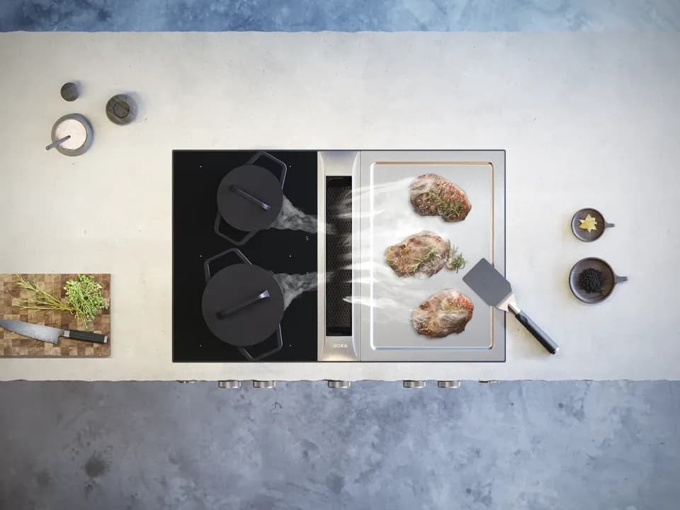 Moderne Küche mit Schmortopf und Bratpfanne auf dem Herd, dampfendes Essen und Küchenutensilien im Hintergrund.