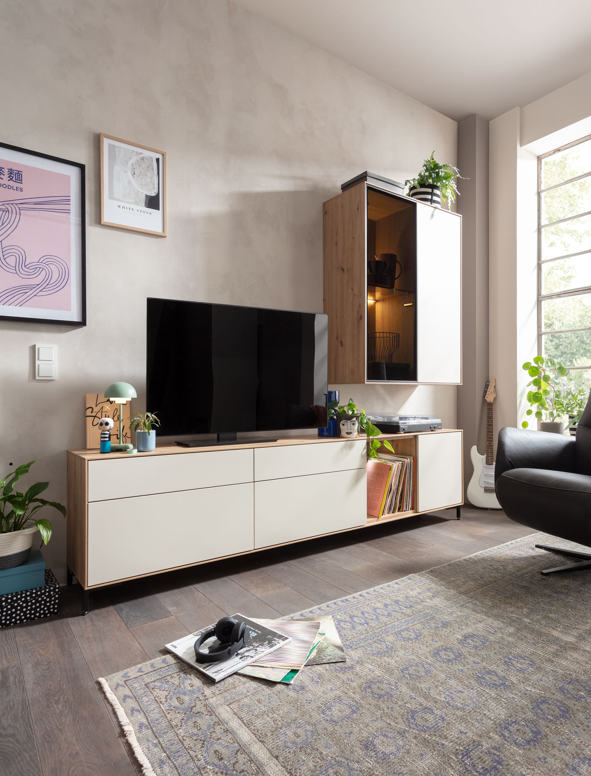 Moderne Wohnzimmereinrichtung mit Fernseher, Couchtisch, Pflanzen und stimmiger Dekoration in heller Atmosphäre.